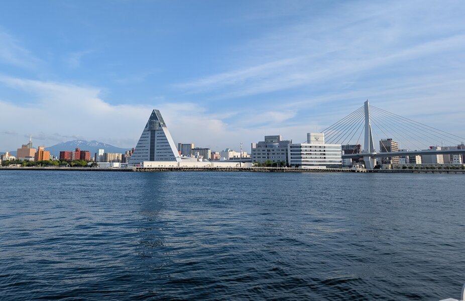 View across the water at Aomori's waterfront, showing the tourism building that's a big triangle, and the A-shaped arches of a bridge going over downtown.